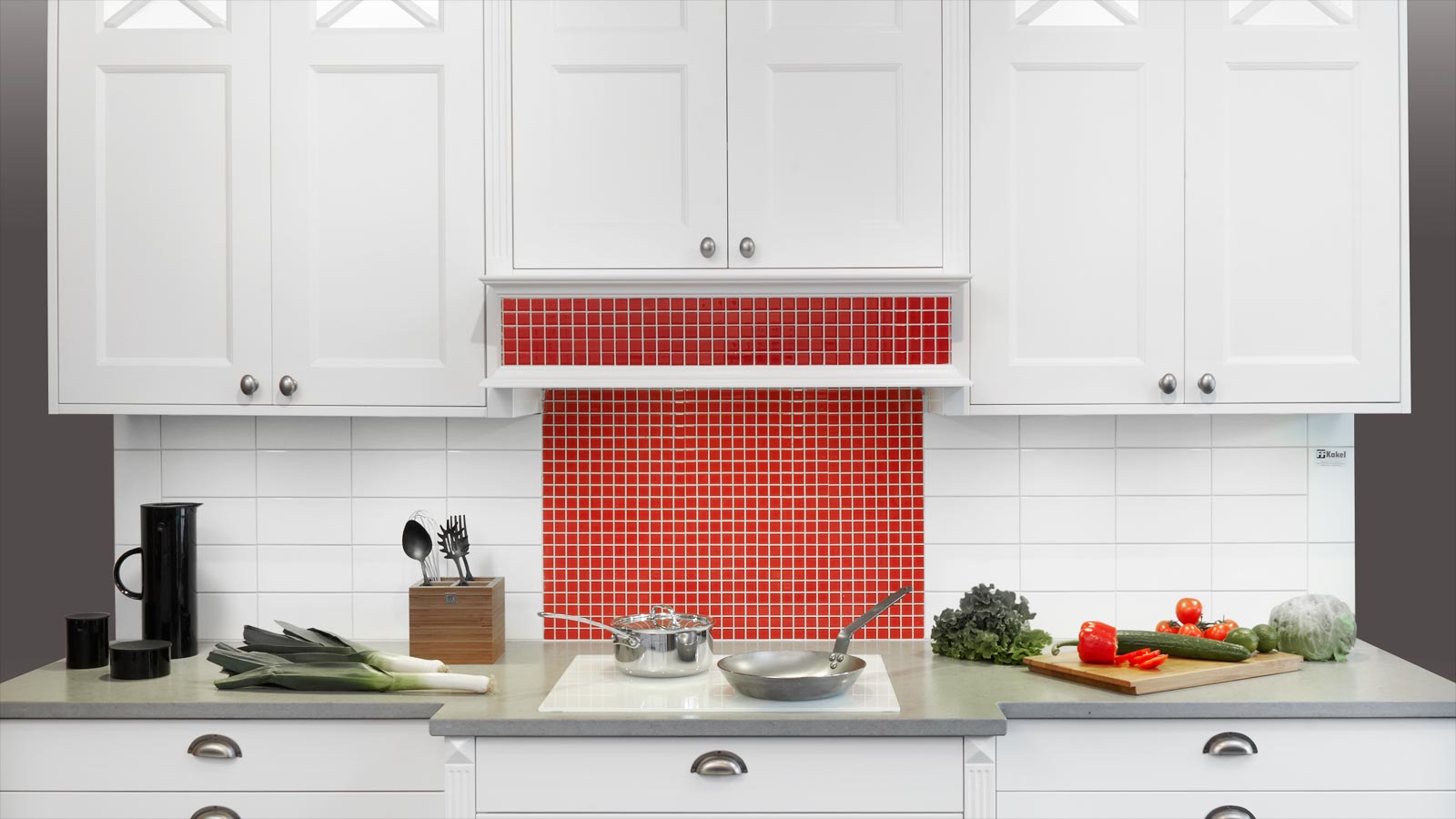 Hos Smartkök Malmö hittar du nya köksluckor till ett bra pris. Exempelbild på ett klassiskt vitt kök med fasade luckor och silverfärgade handtag,. Kakel med små röda rutor på väggen bakom spisen och vitt kakel med rektangulära rutor båda sidor om det röda. kaklet.