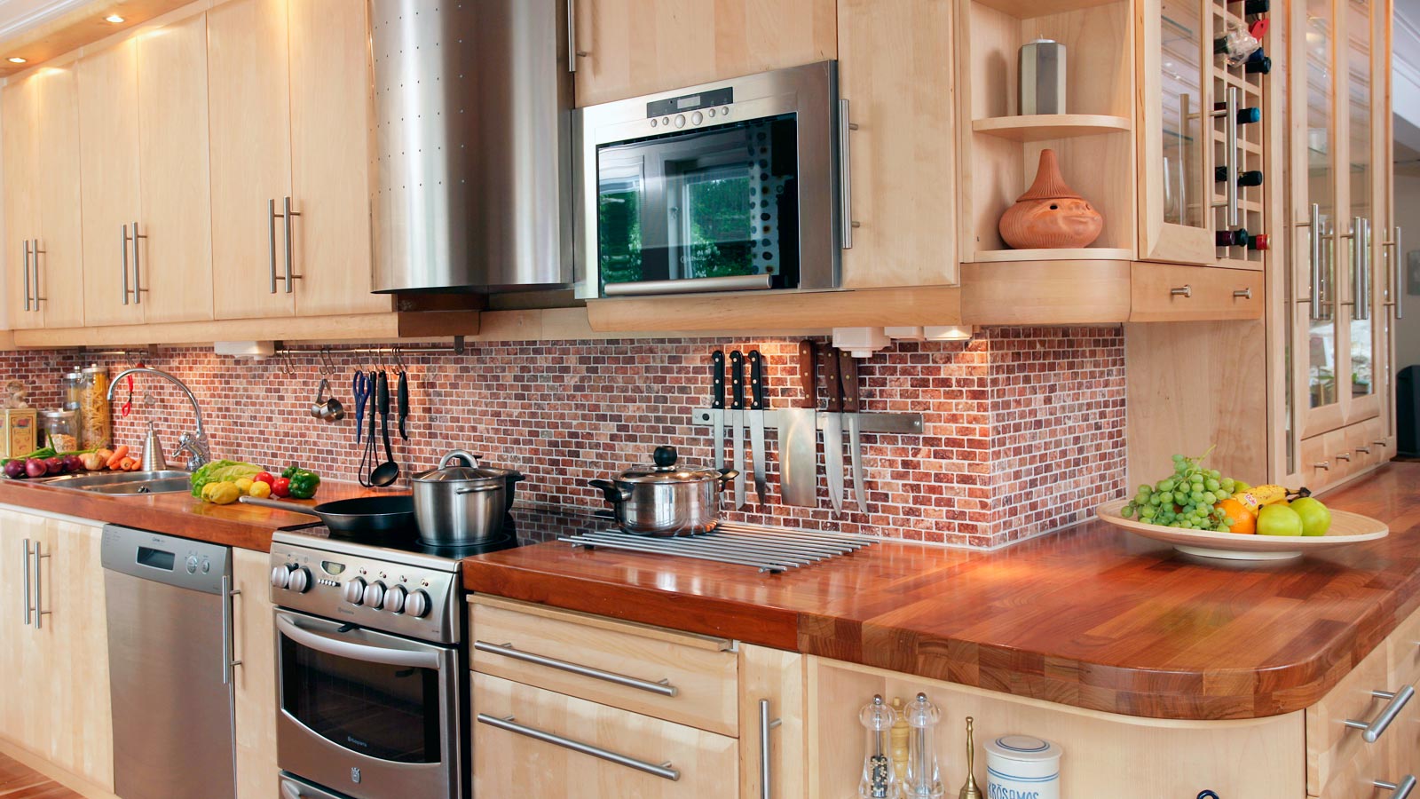 Nya köksluckor hittar du på Smartkök till ett bra pris. Exempelbild på ett lantligt kök i ljust trä med stilrena handdtag och fasade luckor. Kakel med små rektangulära rutor som går i bruna/mörkröda toner, och en bänkskiva i massivt trä.